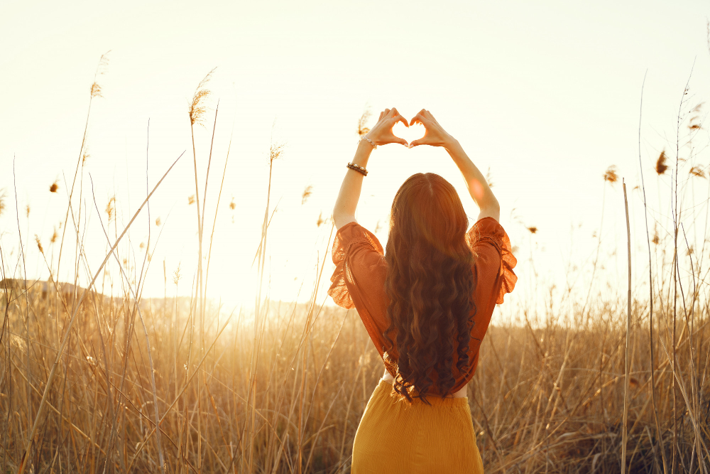 Mujer haciendo un corazón con sus manos a contra luz en un prado