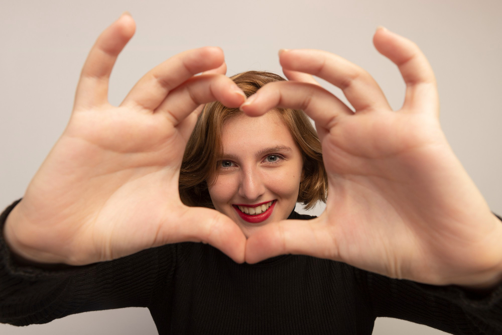 Mujer haciendo un corazón con sus manos, sonriendo y haciéndote saber lo valiosa que eres y lo valioso de tu amor propio autoestima saludable