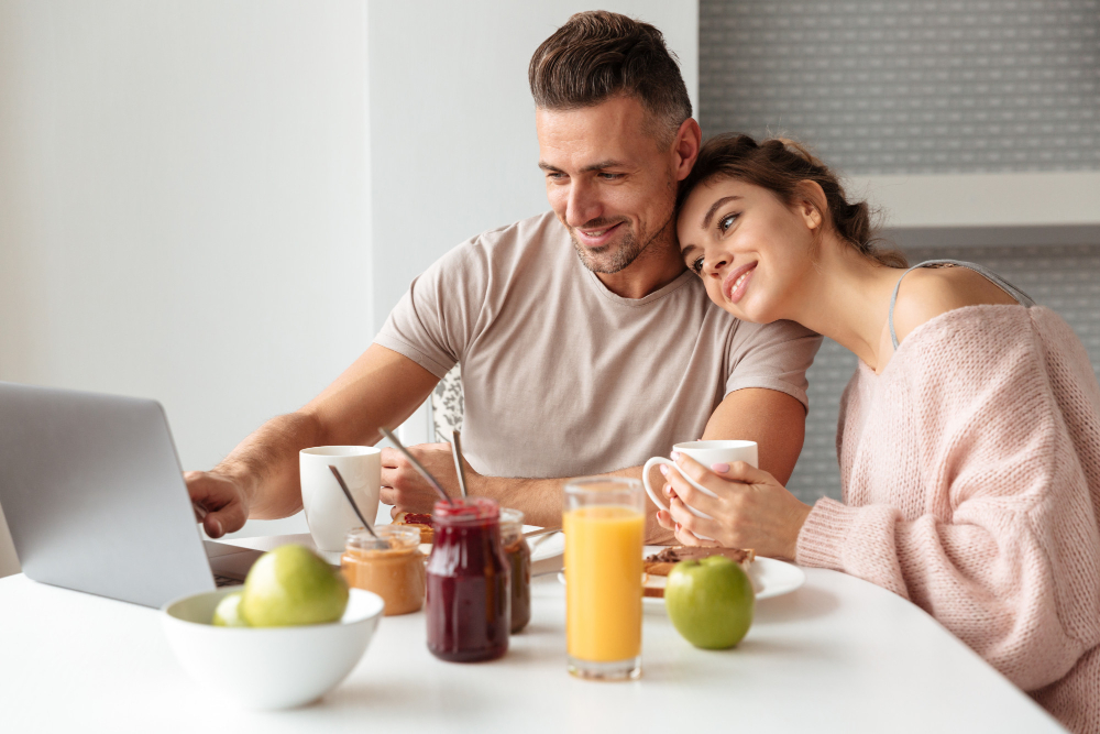 Pareja feliz abrazada mientras ven su ordenador y comen comida saludable